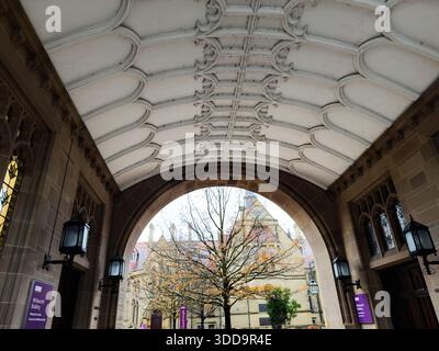 Manchester, Großbritannien - 06. Dezember 2025: Historischer Torbogen-Korridor in Manchester mit verzierten Decken, Laternen und einem Baum, der durch den Bogen sichtbar ist. Stockfoto