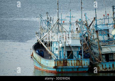 Alte verwitterte blaue Fischerboote mit rostigen Metallrümpfen, die am Hafendock mit traditioneller Takelage-Ausrüstung für die kommerzielle Fischerei ankern Stockfoto