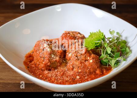 Fleischbällchen, serviert über Tomatensauce in einer weißen Schüssel, garniert mit gekeimtem Gemüse und Parmesankäse, serviert als herzhafte hausgemachte Mahlzeit Stockfoto