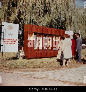 Slawjansk, Ukraine, UdSSR, 1980er Jahre Die Bewohner sehen während des Herbstfestes auf dem Puschkin Boulevard eine Freiluftausstellung der Slawjansk Furniture Factory. Eine massive polierte Holzwand mit Glasschränken und Porzellangeschirr steht auf dem Gras unter Weiden. Die Ausstellung gehört dem Verein Donetskmebel, der nach dem 26. KPdSU-Kongress benannt wurde. Die Bürger besichtigen die sowjetische Innenarchitektur und Konsumgüter und heben die industriellen Errungenschaften und das tägliche Leben der Stadt hervor. Stockfoto