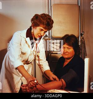 Slawjansk, Ukraine, UdSSR, 1980er Jahre Eine Ärztin misst den Blutdruck eines Patienten im Bogatyr-Präventivorium der Khimprom-Anlage. Der Arzt in einem weißen Fell verwendet ein manuelles Sphygmomanometer und Stethoskop, um die Gesundheit der Frau während einer Routineuntersuchung zu überprüfen. Die Szene findet in einem mit Rehabilitationsgeräten ausgestatteten medizinischen Raum statt. An diesem Standort wurden regelmäßige Kontrollen und Behandlungen für Industriearbeiter durchgeführt. Das Archivbild zeigt die aufmerksame medizinische und soziale Unterstützung der Mitarbeiter in der friedlichen Sowjetstadt. Stockfoto