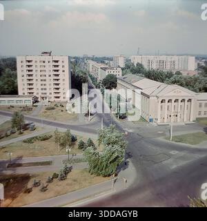 Slawjansk, Ukraine, UdSSR, 1980er Jahre Ein Panoramablick aus einem hohen Winkel mit Blick auf die landwirtschaftliche Technische Hochschule in der Chubar-Straße (heute Swetlodarskaya-Straße). Das Bildungsgebäude verfügt über einen klassischen Säulengang, der im Kontrast zum modernen neunstöckigen Wohnblock aus weißem Backstein auf der anderen Straßenseite steht. Die breiten Straßen sind ruhig mit minimalem Verkehr, umgeben von grünen Rasenflächen und jungen Tannen. Dieses Archivbild erfasst die Stadtplanung, die Bildungsinfrastruktur und die friedliche Atmosphäre der sowjetischen Donbass-Stadt. Stockfoto