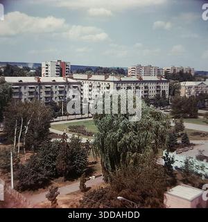 Slawjansk, Ukraine, UdSSR, 1980er Jahre Erhöhter Panoramablick auf das Stadtzentrum vom Steuergebäude aus. Die Aufnahme erfasst den Platz der Oktoberrevolution (heute Soborna Square) und die Lenin Street (heute University St). Sowjetische Propaganda-Slogans "Frieden für die Welt" (Miru mir) und "Ruhm für die KPdSU" (Slava KPSS) sind auf den Dächern von Wohnziegelbauten zu sehen. In der Gegend gibt es üppiges Grün, große Weiden und Bürger, die entlang der Alleen spazieren. (558 знаков — идеально, почти предел). Stockfoto