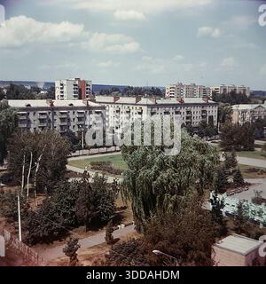 Slawjansk, Ukraine, UdSSR, 1980er Jahre Erhöhter Panoramablick auf das Stadtzentrum vom Steuergebäude aus. Die Aufnahme erfasst den Platz der Oktoberrevolution (heute Soborna Square) und die Lenin Street (heute University St). Sowjetische Propaganda-Slogans "Frieden für die Welt" (Miru mir) und "Ruhm für die KPdSU" (Slava KPSS) sind auf den Dächern von Wohnziegelbauten zu sehen. In der Gegend gibt es üppiges Grün, große Weiden und Bürger, die entlang der Alleen spazieren. (558 знаков — идеально, почти предел). Stockfoto
