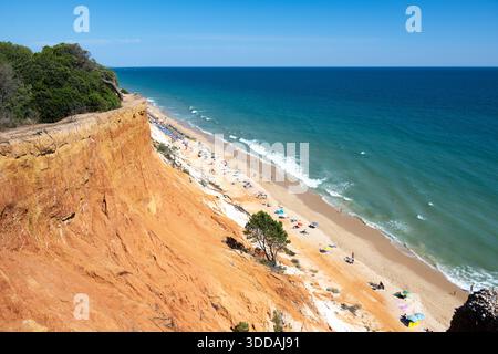 Ein malerischer Blick auf den Strand Praia Santa Eulalia mit goldenen Klippen und türkisfarbenem Wasser, gesäumt von Sonnenanbetern und Sonnenschirmen Stockfoto