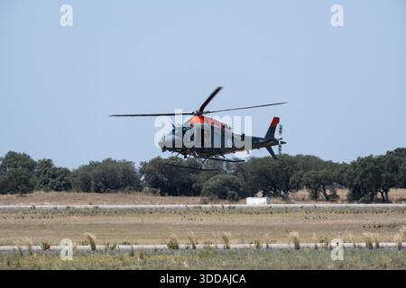 Beja, Portugal - 18. Juni 23: Ein Hubschrauber fliegt über einem grasbewachsenen Flugplatz mit Bäumen im Hintergrund Stockfoto