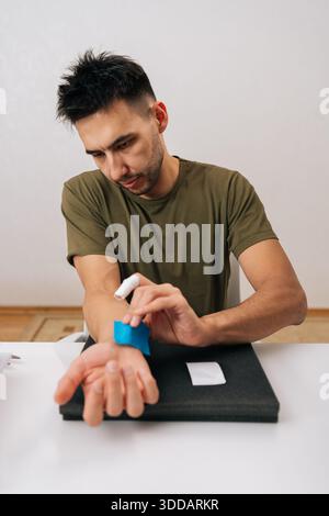 Vertikales Porträt eines Mannes, der blaues elastisches therapeutisches Band am Handgelenk zur Linderung von Muskel- und Gelenkschmerzen aufträgt und die Erholung von Verletzungen oder Belastungen unterstützt; Stockfoto