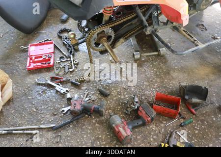 Hochwinkelaufnahme eines kaputten Fahrzeugs in Reparatur, das Mechaniker auf nassem Betonboden mit schmutzigem Teil und zerlegtem, rostigem Quad im Chaoti zeigt Stockfoto