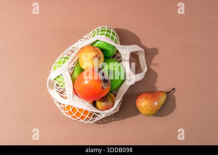 Verschiedene Früchte in einem Netzbeutel auf brauner Oberfläche mit einfacher natürlicher Lebensmittelanordnung. Null-Abfall-Konzept. Draufsicht. Stockfoto