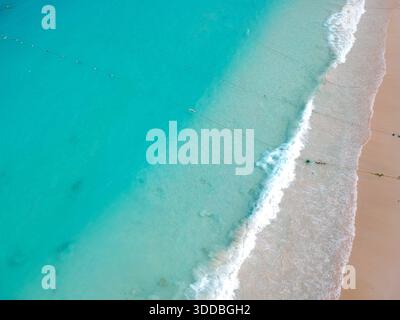 Von oben aus blickt man auf einen unberührten Strand mit türkisfarbenem Wasser, weißen Schaumwellen und Menschen, die die Sommersonne genießen. Stockfoto