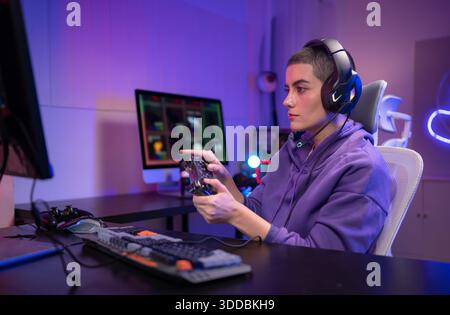Ein fokussierter Gamer sitzt am Schreibtisch und tippt auf einer mechanischen Tastatur in einem neonbeleuchteten Gaming-Setup. Wenn sie ein Headset um den Hals tragen, sehen sie selbstbewusst aus, während sie sich an einem PC-Gaming oder Streaming-Aktivitäten beteiligen || Modell veröffentlicht Stockfoto
