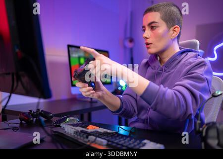 Ein fokussierter Gamer sitzt am Schreibtisch und tippt auf einer mechanischen Tastatur in einem neonbeleuchteten Gaming-Setup. Wenn sie ein Headset um den Hals tragen, sehen sie selbstbewusst aus, während sie sich an einem PC-Gaming oder Streaming-Aktivitäten beteiligen || Modell veröffentlicht Stockfoto