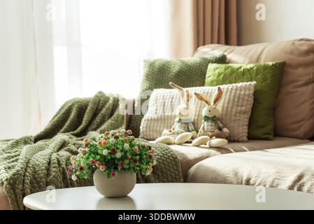 Gemütliches Oster-Wohnzimmer mit Plüschpuppen des Osterhasen und Frühlingsblumen auf dem Tisch Stockfoto