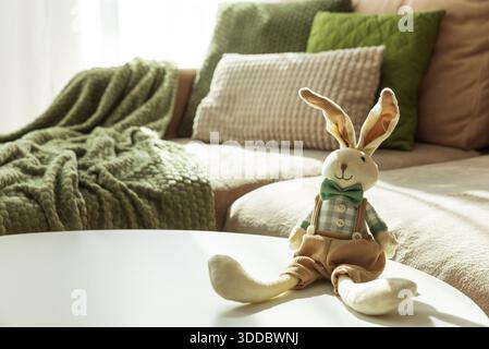 Gemütliches Oster-Wohnzimmer mit Plüschpuppen des Osterhasen und Frühlingsblumen auf dem Tisch Stockfoto