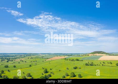 Panoramablick aus der Vogelperspektive auf üppige grüne Wiesen, verstreute Bäume und Fleckenbebauung mit einem sanften bewaldeten Hügel unter einem hellblauen Himmel in der Landschaft des Nivernais. Stockfoto