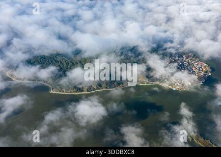 Aus der Vogelperspektive fängt die Insel Ioannina ein, die zum Teil von treibendem Morgennebel bedeckt ist, mit dichtem Wald und einer Ansammlung von Häusern am See, umgeben von ruhigem Wasser in Epirus, Griechenland. Weiche Wolkendecke und natürliche Texturen sorgen für eine ruhige, atmosphärische Szene. Stockfoto