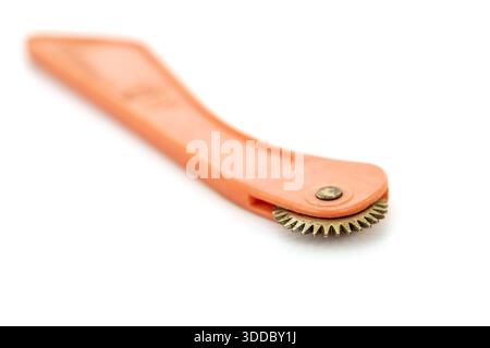 Ein Vintage-Tastrad, das zum Markieren von Mustern auf Stoff verwendet wird, steht vor einem sauberen weißen Hintergrund. Das Werkzeug verfügt über einen orangefarbenen Griff und eine Wende Stockfoto