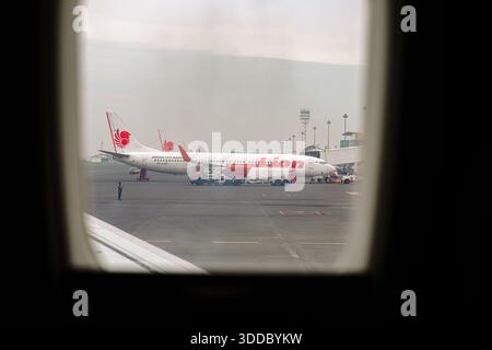 Ansicht von einem Flugzeugfenster mit mehreren Lion Air Boeing 737-900ER Flugzeugen, die auf dem Rollfeld geparkt sind. Ein Tankwagen und die Bodencrew warten ein Flugzeug. A Stockfoto