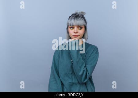 Junge Frau mit grauem Haar in lässigem Pullover, nachdenkliche Pose. Stockfoto