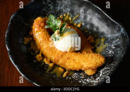 Ein Teller mit einer Banane und Eis drauf. Die Banane ist mit Puderzucker bedeckt und das Eis wird mit Karamellsauce getränkt. Das Gericht Stockfoto