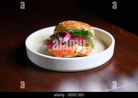 Ein Sandwich mit Zwiebeln und Dill auf einem weißen Teller. Das Sandwich wird auf einen Holztisch gestellt Stockfoto