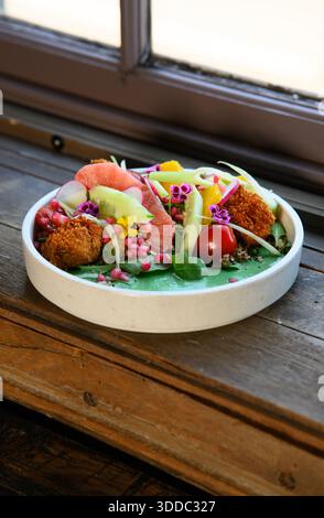 In einer weißen Schüssel wird ein farbenfroher Salat mit einer Vielzahl von Gemüse und Früchten, einschließlich Tomaten, Gurken und Karotten, serviert. Die Schüssel wird aufgesetzt Stockfoto