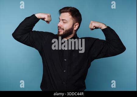 Mann in schwarzem Hemd, der Muskeln vor blauem Hintergrund beugt. Stockfoto