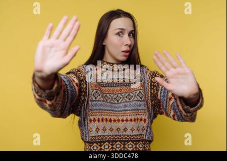 Frau in gemustertem Pullover mit erhobenen Händen auf gelbem Hintergrund. Stockfoto