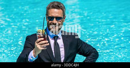 Sommerreisen. Geschäftserfolg. Geschäftsmann in Anzug im Swimmingpool. Aufgeregter Geschäftsmann im Nassanzug im Schwimmbad. Remote-Arbeiten. Geschäftsgetränk Stockfoto