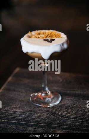 Ein Glas braune Flüssigkeit mit weißem Schaum oben. Der Schaum ist mit Schokolade getränkt Stockfoto