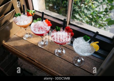 Vier verschiedene Cocktails in Martini-Gläsern mit Eis und Garnituren. Die Cocktails stehen hintereinander auf einem Holztisch Stockfoto