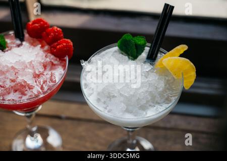 Zwei Getränke mit Strohhalmen, eines ist ein rosafarbenes Getränk mit Himbeeren und das andere ein weißes Getränk mit einer Zitronenscheibe Stockfoto