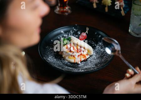 Eine Frau isst ein Dessert mit einem Löffel. Das Dessert besteht aus einem Bananenaufschnitt mit Schlagsahne und Erdbeeren Stockfoto