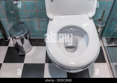 Saubere, weiße Toilettenschüssel mit eingebauter Bidet-Düse, Metallmüll und geprüfte Bodenfliesen in einem modernen WC Stockfoto