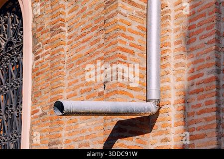 Rote Ziegelwand mit Metallfallrohr und Teil eines dekorativen schmiedeeisernen Fensters Stockfoto