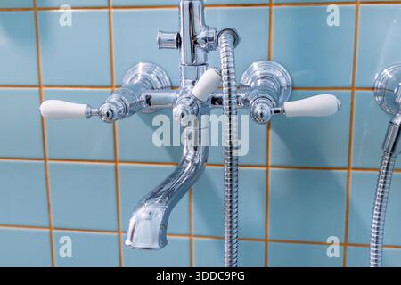 Chrom-Armatur im Vintage-Stil mit weißen Keramikgriffen an der blau gefliesten Wand im Badezimmer Stockfoto