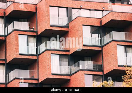 Wohngebäude in modernem Design mit mehreren Balkonen, Glasgeländern und rotem Backsteinfassement Stockfoto
