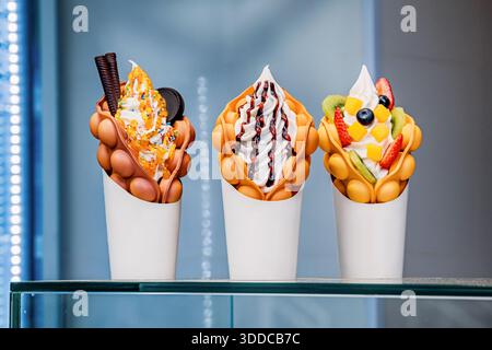 Süße Waffeln gefüllt mit weichem Serviereis und verschiedenen Belägen einschließlich Obst, Saucen und Plätzchen Stockfoto