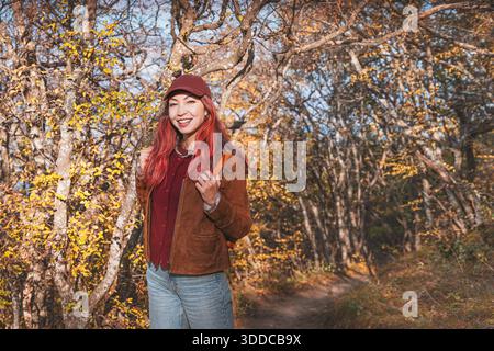 Frau lächelt und trägt einen Rucksack und genießt eine Wanderung im Freien auf einem Waldweg mit wechselnden Herbstblättern Stockfoto
