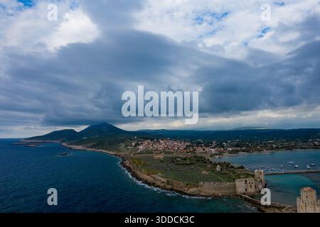 Blick aus der Vogelperspektive auf die Burg Methoni, die sich entlang der zerklüfteten griechischen Küste erstreckt, mit dramatischen Sturmwolken darüber und dem Dorf zwischen Meer und Bergen. Stockfoto