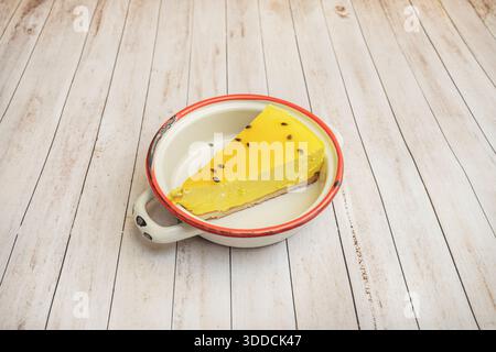 Dreieckige Scheibe gebackener New Yorker Käsekuchen mit goldener Kruste und cremiger Mitte, serviert mit Himbeersauce und frischen Minzblättern auf einer schwarzen Platte Stockfoto