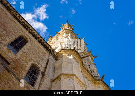 Blick nach oben auf einen kunstvoll verzierten gotischen Kirchturm mit kunstvollen Wasserspeiern und komplizierten Steinschnitzereien vor einem leuchtend blauen Himmel in Nevers. Das Bild zeigt historische Architektur, strukturiertes Mauerwerk und dramatisches Sonnenlicht auf detaillierten Fassaden. Stockfoto