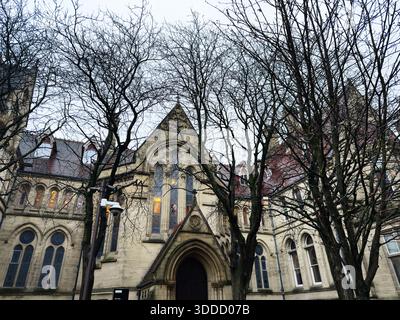 Manchester, Großbritannien - 06. Dezember 2025: Steinkirche in Manchester mit blattlosen Bäumen, die eine stimmungsvolle urbane Szene schaffen. Stockfoto