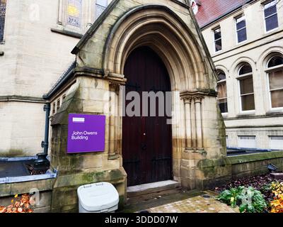 Manchester, Großbritannien - 06. Dezember 2025: Historischer Eingang zum John Owens Building auf dem Manchester Campus mit großer Holztür und lila Schild. Stockfoto