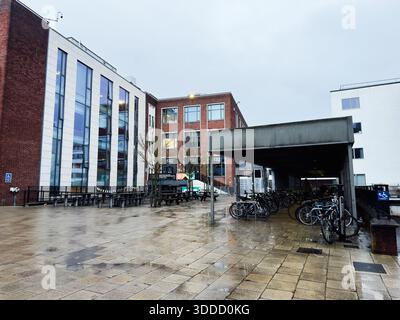 Manchester, Großbritannien - 06. Dezember 2025: Modernes Universitätsgebäude aus Backstein und Glas mit überdachtem Fahrradbereich und nassem Gehweg. Stockfoto