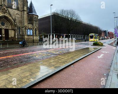 Manchester, Großbritannien - 06. Dezember 2025: Historische Kirche und moderne Gebäude säumen eine regendurchflutete Manchester Street. Stockfoto