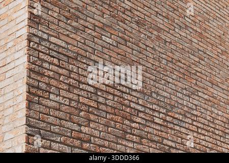 Die Gebäudewand zeigt zwei Seiten, die sich an einer Ecke treffen, und erzeugt ein strukturiertes Muster aus verschiedenen roten und beigen Ziegeln Stockfoto