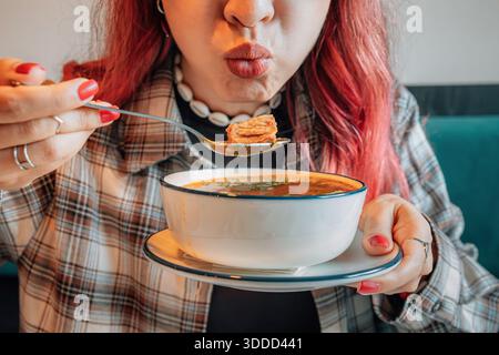 Eine junge Frau genießt eine herzhafte georgianische Kharcho-Suppe während des Mittagessens und bläst auf einen Löffel Essen Stockfoto