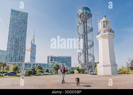 6. November 2025, Batumi, Georgia: Person, die einen Hund entlang der Promenade mit dem alphabetischen Turm und dem Leuchtturm führt Stockfoto