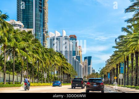 Sunny Isles Beach, USA - 30. April 2024: Florida Road Collins Avenue Street in Miami, Florida mit Autos durch Wohngebäude und Palmen sonnigen Tag Stockfoto